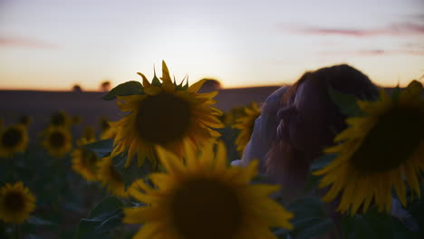 Young-Female-Poses-with-Sunflowers-in-Field-on-Late-Summer-Evening,-medium-shot