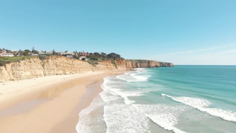 Ocean-waves-gently-unfolding-on-golden-Porto-de-Mós-beach,-Lagos,-Algarve,-Portugal---Aerial-Ground-Level-fly-over-shot