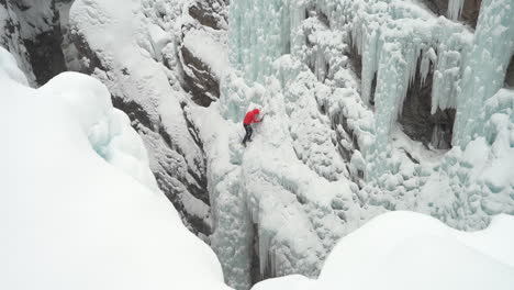 Ice-climber-climbing-on-frozen-waterfall-in-snowy-winter-landscape-of-Ouray-Ice-Park,-Colorado-USA,-wide-view