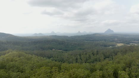 Wide-View-Of-Mountains-Tibberoowuccum,-Tibrogargan,-Cooee,-Beerwah,-Coonowrin-And-Ngungun-Across-Pine-Forest-In-Glass-House-Mountains-Region-In-Queensland,-Australia---aerial-drone-shot