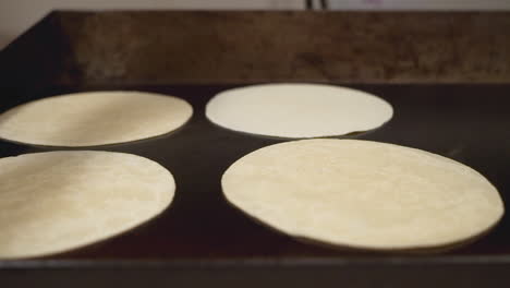 Kitchen-worker-cooks-flour-tortillas-on-hot-flat-top-griddle,-slow-motion-trucking-shot-HD
