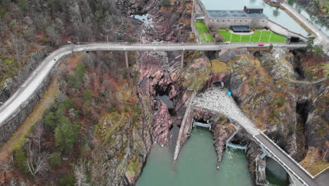 Aerial-pull-out-shot-of-vehicles-driving-on-the-corniche-cliffside-Oskarsbron-Oskar-bridge-at-Trollhättan-waterfalls-and-locks-in-Sweden