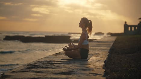 Woman-in-yoga-lotus-pose-meditating-at-tropical-shore-during-sunset,-dusk