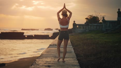 Woman-completely-zen,-mind-and-body-doing-yoga-tree-pose-during-bright-sunset