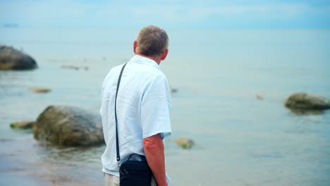 An-Old-Man-Looking-At-The-Sea-In-Karkle-Beach,-Lithuania---medium-shot
