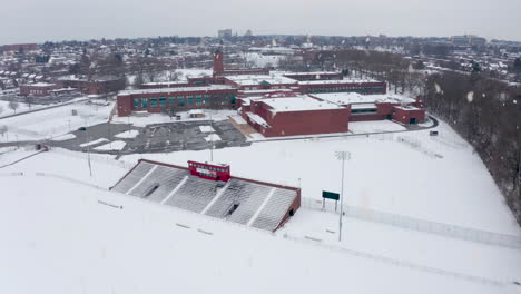Winter-snow-on-school-building-and-stadium,-athletic-fields