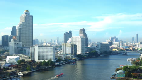 BANGKOK,-THAILAND-2021---Boats-and-ships-on-wide-fast-Chao-Phraya-river-with-high-skyscrapers-buildings-on-the-river-banks-daytime-timelapse