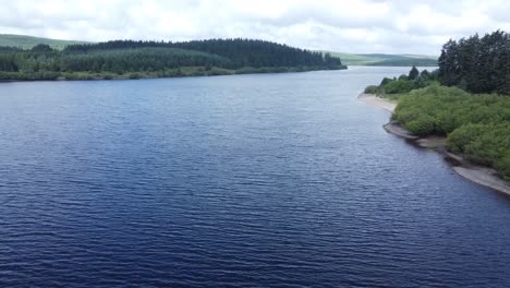 Idyllic-blue-water-reservoir-lake-woodland-hiking-walk-aerial-view-pull-back-reservoir-tower-reveal