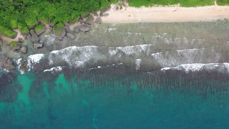 Spectacular-aerial-ascending-shot-straight-down-view-capturing-beautiful-turquoise-sea-water-with-waves-crashing-the-rocky-shore-at-Xiaoliuqiu-Lambai-Island,-Pingtung-county,-Taiwan