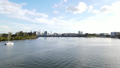 Catamaran-Boats-Adrift-On-Water-Surface-Of-Brisbane-River-With-Brisbane-CBD-Skyline-In-Distance