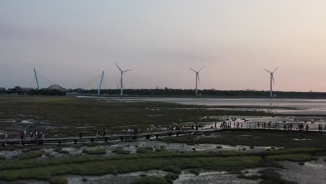 Cinematic-aerial-tracking-shot-at-Gaomei-wetlands-preservation-area-with-wind-turbines-spinning-and-rotating-at-the-horizon-at-sunset,-Taichung,-Taiwan
