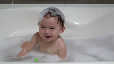 Pequeña-Niña-De-Un-Año-De-Etnia-Mixta-Que-Disfruta-Tomando-Un-Baño-Con-Espuma-Mostrando-Felizmente-Una-Sonrisa-Con-Dientes-Mientras-Tiene-Espuma-En-El-Cabello-Mojado-En-La-Bañera-En-Casa