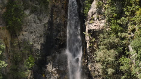 Tilt-down-shot-of-idyllic-waterfall-falling-down-rocky-wall-in-national-park-of-New-Zealand-during-summer