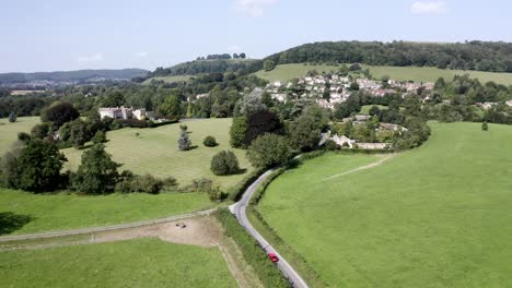 AERIAL---Stouts-Hill,-houses-and-hills-in-Uley,-Cotswolds,-England,-wide-forward