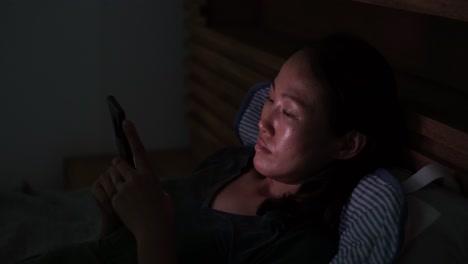 Asiatische-Frau,-Die-Auf-Dem-Smartphone-Zuschaut,-Während-Sie-Sich-Nachts-Im-Bett-Ausruht