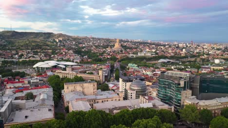 Aerial:-Tbilisi-at-sunset-with-The-Holy-Trinity-Cathedral-in-background,-Georgia