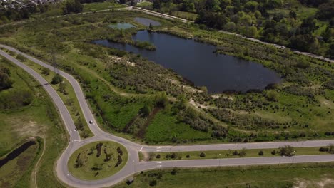 Aerial-view-of-roundabout-near-small-lake-in-countryside,-Buenos-Aires-province