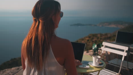 Slow-dolly-zoom-in-of-beautiful-luxury-girl-working-on-laptop-with-epic-ocean-view-during-sunlight
