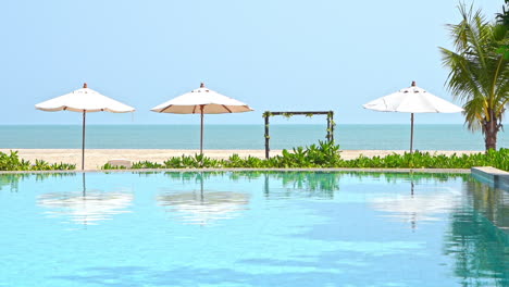 Sandstrand-Resort-Mit-Meerblick-Und-Sonnenschirmen,-Die-Auf-Einem-Leeren-Infinity-Pool-Reflektieren