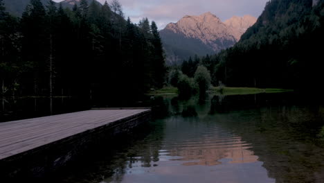Alpine-mountain-lake-at-sunset,-Plansar-or-Plansarsko-jezero-in-Jezersko,-Slovenia,-wooden-pier-extending-above-the-water,-Kamnik-Savinja-Alps-reflect-in-water-with-ripples