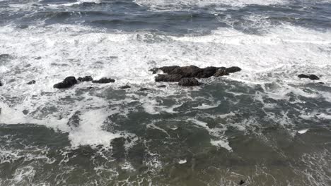 Aerial-forward-over-ocean-waves-breaking-on-sandy-beach-at-Seal-Rock,-Oregon