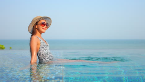 Junge-Asiatische-Mädchen-Lächelt-Entspannend-Im-Infinity-Pool-Mit-Ozean-Im-Hintergrund