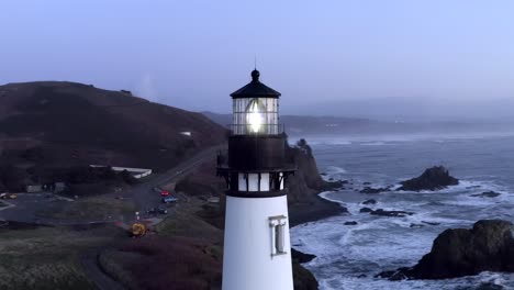 Yaquina-Head-Lighthouse-on-Oregon-coast-at-sunset-dusk,-aerial-arc-shot