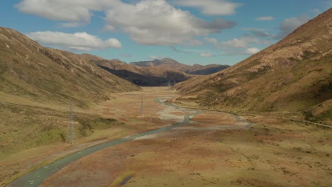 Luftaufnahme-Eines-Wunderschönen-Tals-Mit-Einem-Fluss-Und-Einigen-Hochspannungsmasten-In-Neuseeland