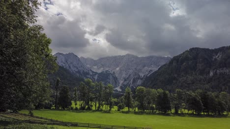Alpine-valley,-Jezersko,-Slovenia,-timelapse-of-clouds-above-mountains-and-meadows-with-trees-in-front