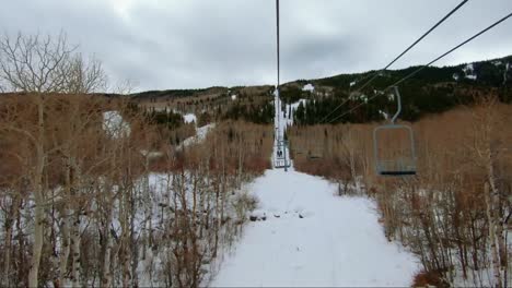 Beautiful-Tilting-up-point-of-view-shot-from-a-ski-lift-at-a-ski-resort-in-Colorado-on-an-overcast-winter-day-with-tall-aspen-and-pine-trees-surrounding-a-clear-snowy-path