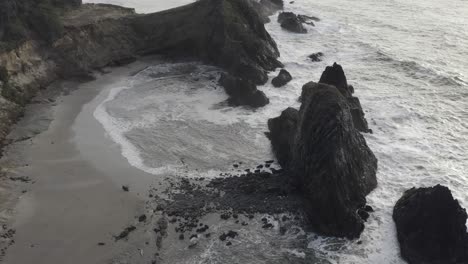 Overcast-day,-Pacific-Ocean-in-Oregon,-aerial-pan-down-over-waves-and-rocks