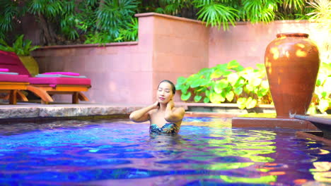 Sexy-Asiatische-Frau,-Die-Haare-Berührt-Und-Ihr-Haar-Im-Schwimmbad-In-Der-Exotischen-Tropischen-Hotellounge-Glättet