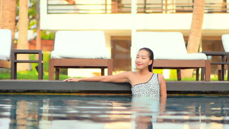A-young-woman-fresh-from-swimming-leans-along-the-edge-of-a-hotel-pool