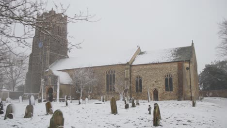Tracking-backwards-away-from-very-old-English-church-covered-in-snow