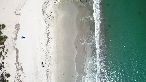 Turquoise-ocean-waves-crashing-onto-a-clean-sandy-beach-and-rocks,-California