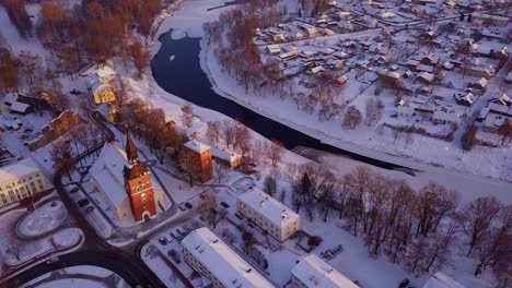 Beautiful-aerial-view-over-Valmiera-during-the-winter,-showing-snowy-houses,-buildings,-river-Gauja-and-church-under-the-warm-glow-of-afternoon-sun