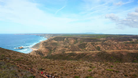 Aerial-circling-shot-showing-group-of-hikers-hiking-on-top-of-Algarve-Coastline-during-beautiful-sunny-day