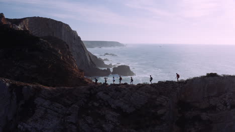 Silhouette-of-active-hiking-group-on-rocky-trail-with-beautiful-algarve-ocean-landscape-in-background-during-sunlight