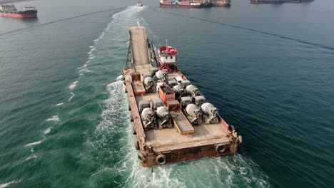Barge-loaded-with-Concrete-mixer-trucks-pulled-to-port-by-a-Tugboat-in-Hong-Kong-bay,-Aerial-view