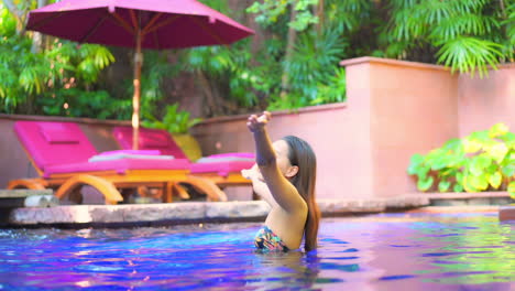 A-pretty-woman-in-a-very-colorful-resort-pool-setting-raises-her-arms-to-the-sky
