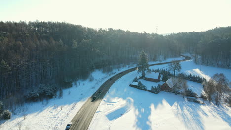 AERIAL-cars-chase,-chasing-shoot-view:-cars-driving-down-an-asphalt-road-crossing-the-vast-forest-on-a-winter-day