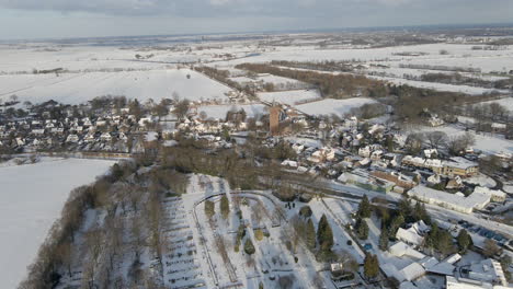 Flying-towards-beautiful-rural-town-surrounded-by-snow-covered-meadows