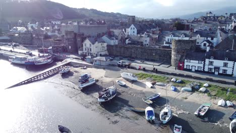 Idyllic-Conwy-castle-and-harbour-fishing-town-boats-on-coastal-waterfront-aerial-drone-dolly-left