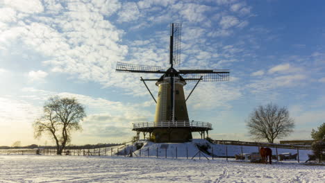 Time-lapse-of-clouds-passing-over-traditional-windmill-in-beautiful-white-winter-rural-landscape---zoom-out