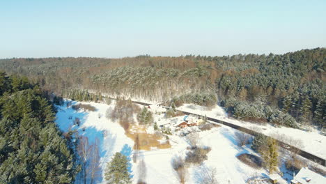 Aerial-forward-shot-of-beautiful-forest-landscape-with-snowy-fields-and-cars-driving-along-asphalt-road