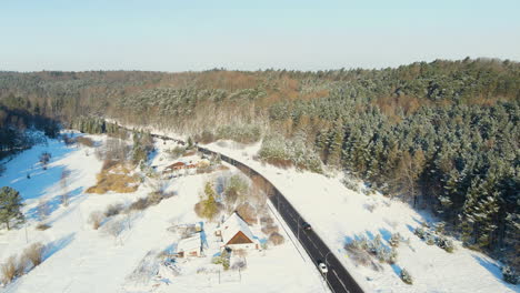 Aerial-view-of-cars-driving-on-icy-road-surrounded-by-winter-snowscape-with-snowdrift-during-sunny-day-in-nature
