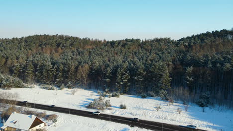 Cars-driving-over-a-black-asphalt-road-with-white-snow-and-in-the-background-giant-pine-tree-forest-on-a-bright-sunny-day-near-Gdansk-Poland