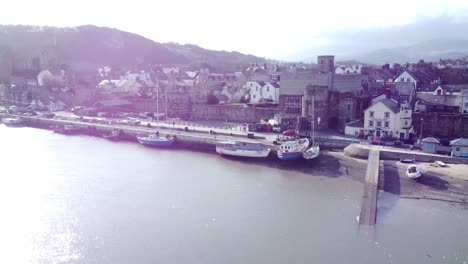 Idyllic-Conwy-castle-and-harbour-fishing-town-boats-on-coastal-waterfront-aerial-rising-pull-back