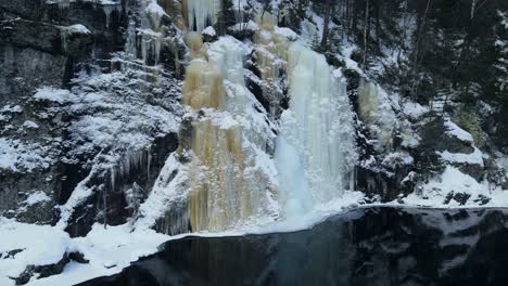 Zooming-out-drone-footage-of-beautiful-frozen-waterfall-that-reflects-in-the-water