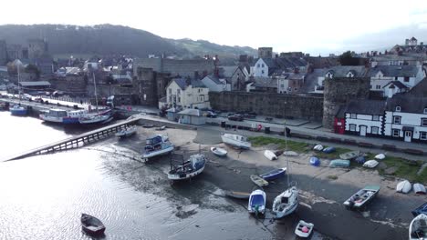 Idyllic-Conwy-castle-and-harbour-fishing-town-boats-on-coastal-waterfront-aerial-descending-push-in